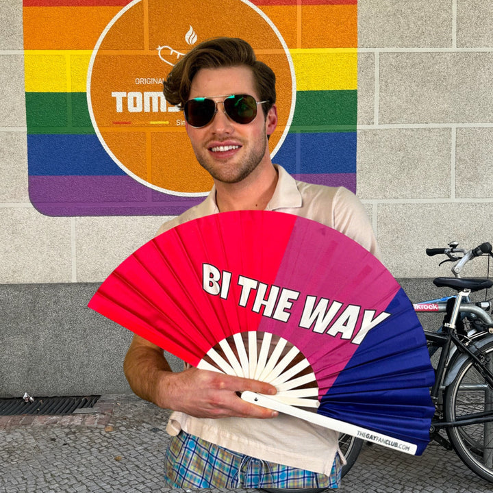 A person holding a large Pride bamboo folding fan wearing sunglasses in Berlin. 